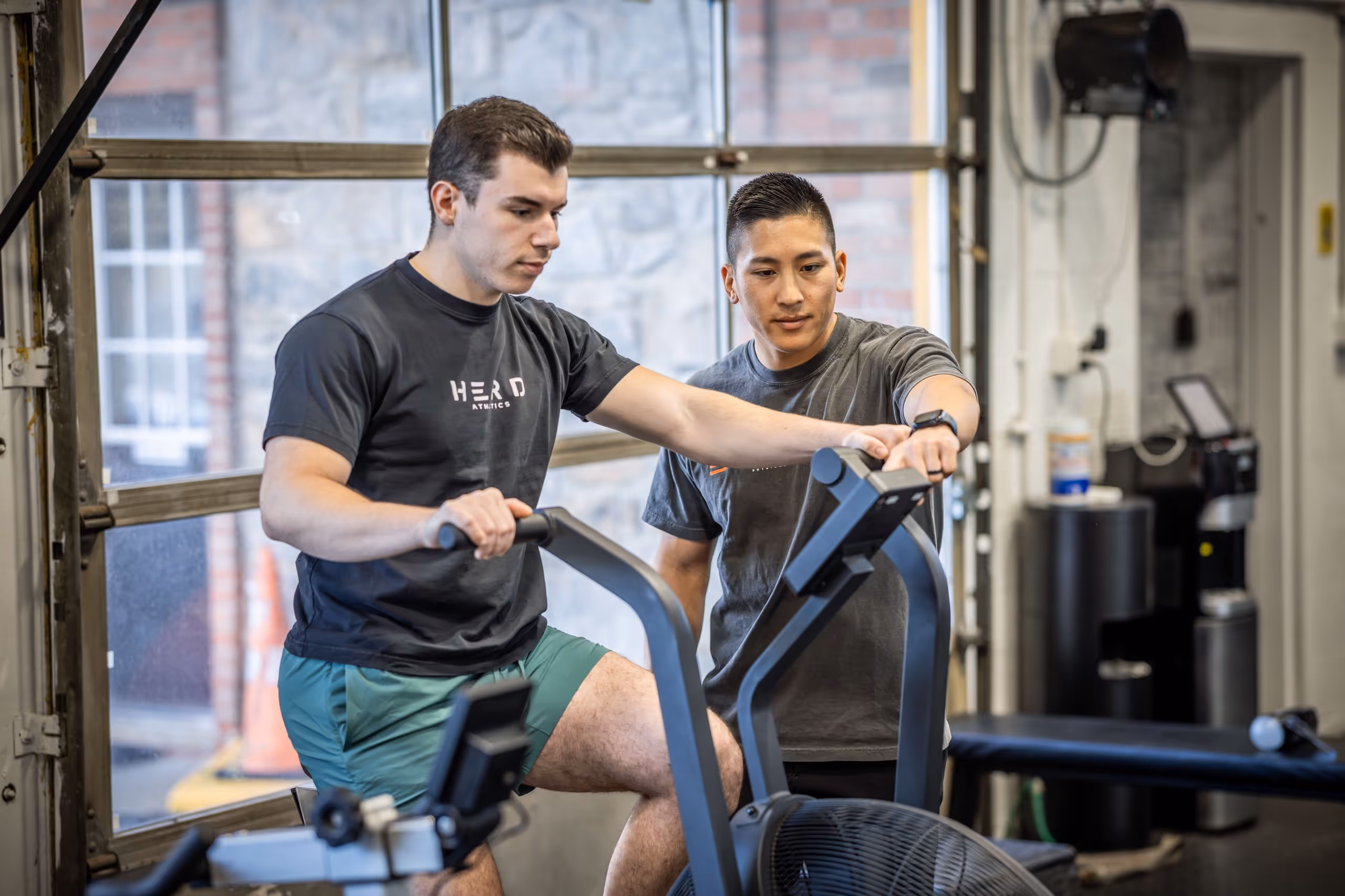 Trainer assisting a man on a stationary exercise bike in a gym. physical therapy massapequa ny