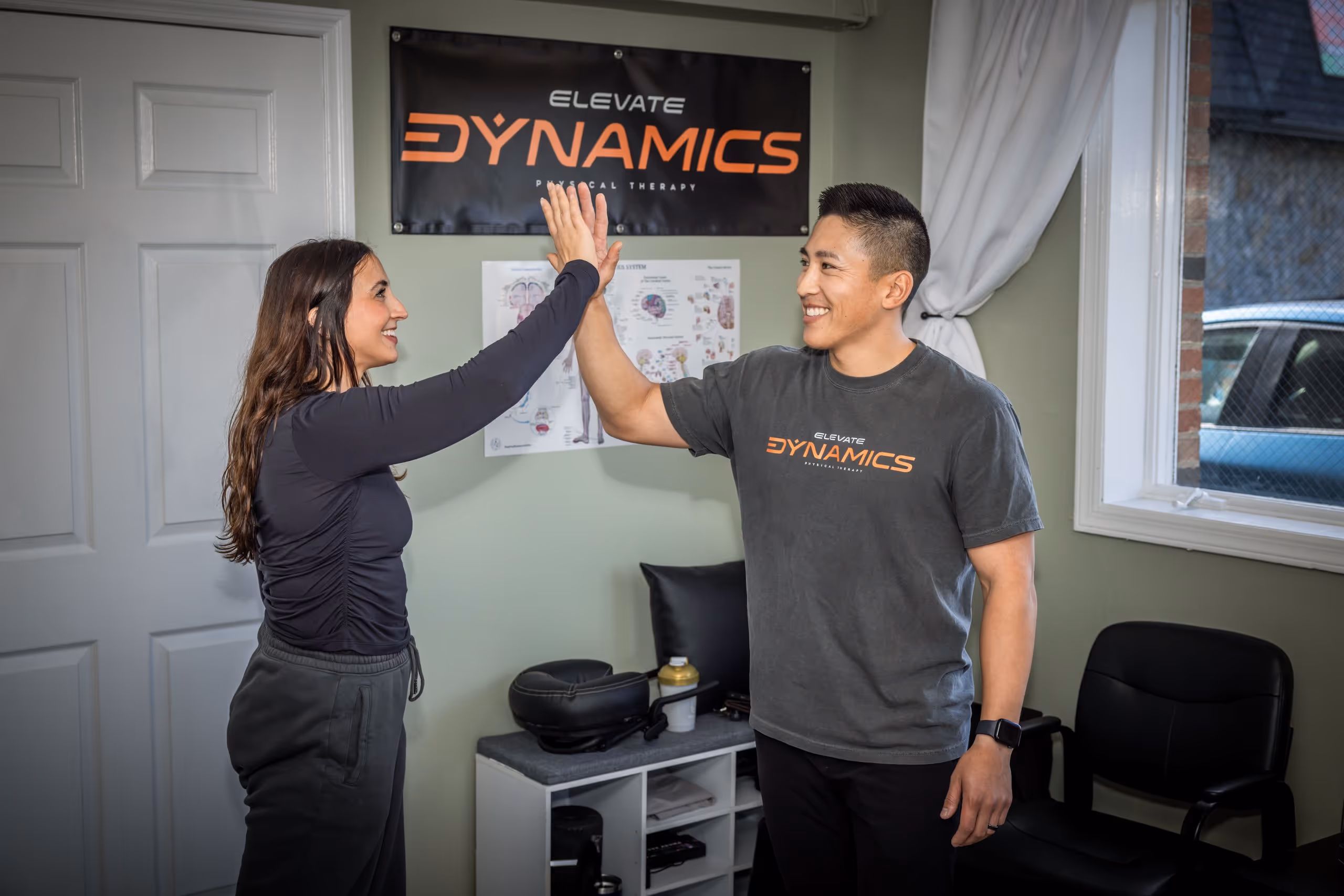 A physical therapist and patient smiling and high-fiving inside a physical therapy clinic in Massapequa, NY.