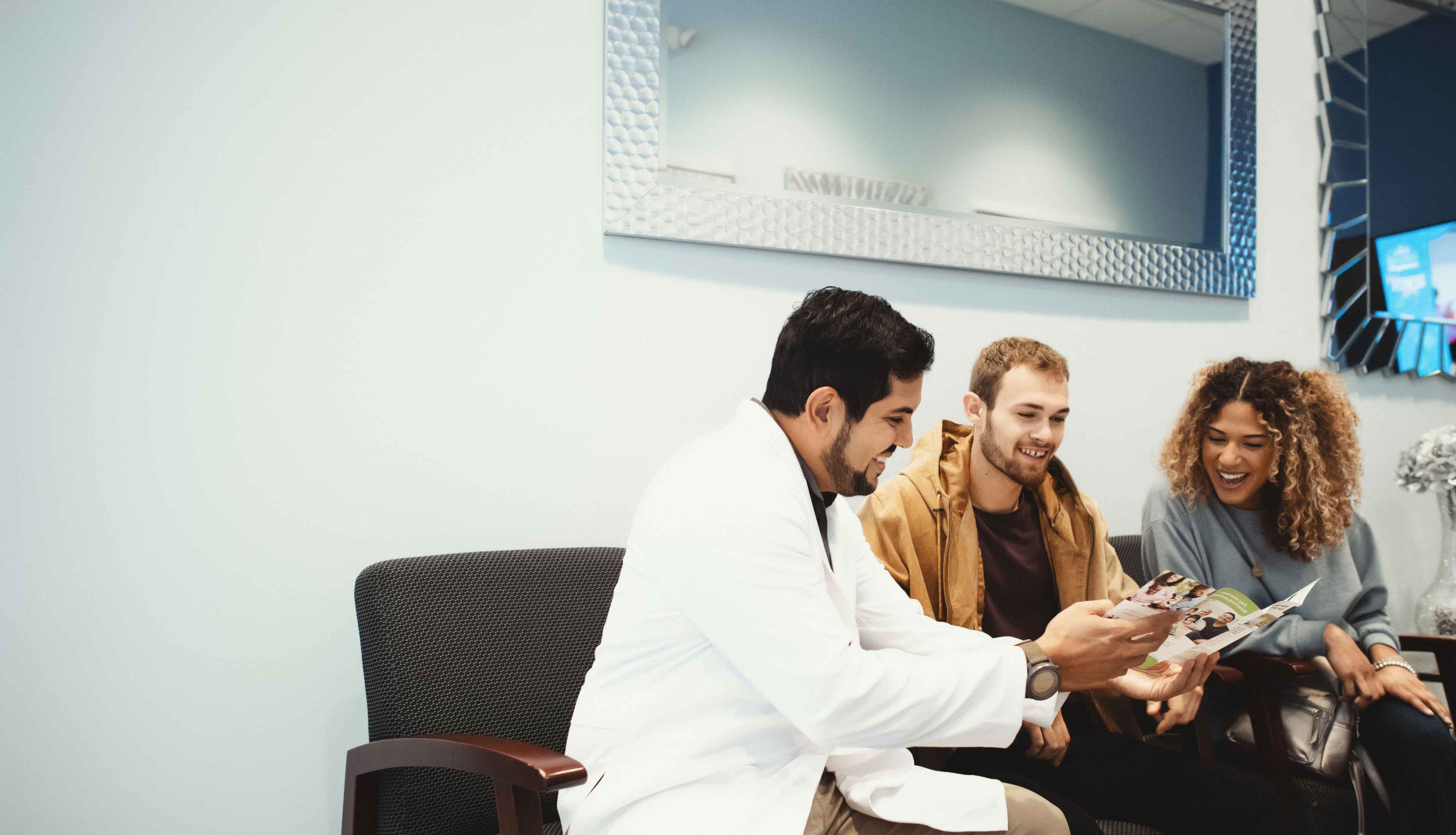 A dentist sitting next to two patients, looking at a treatment booklet