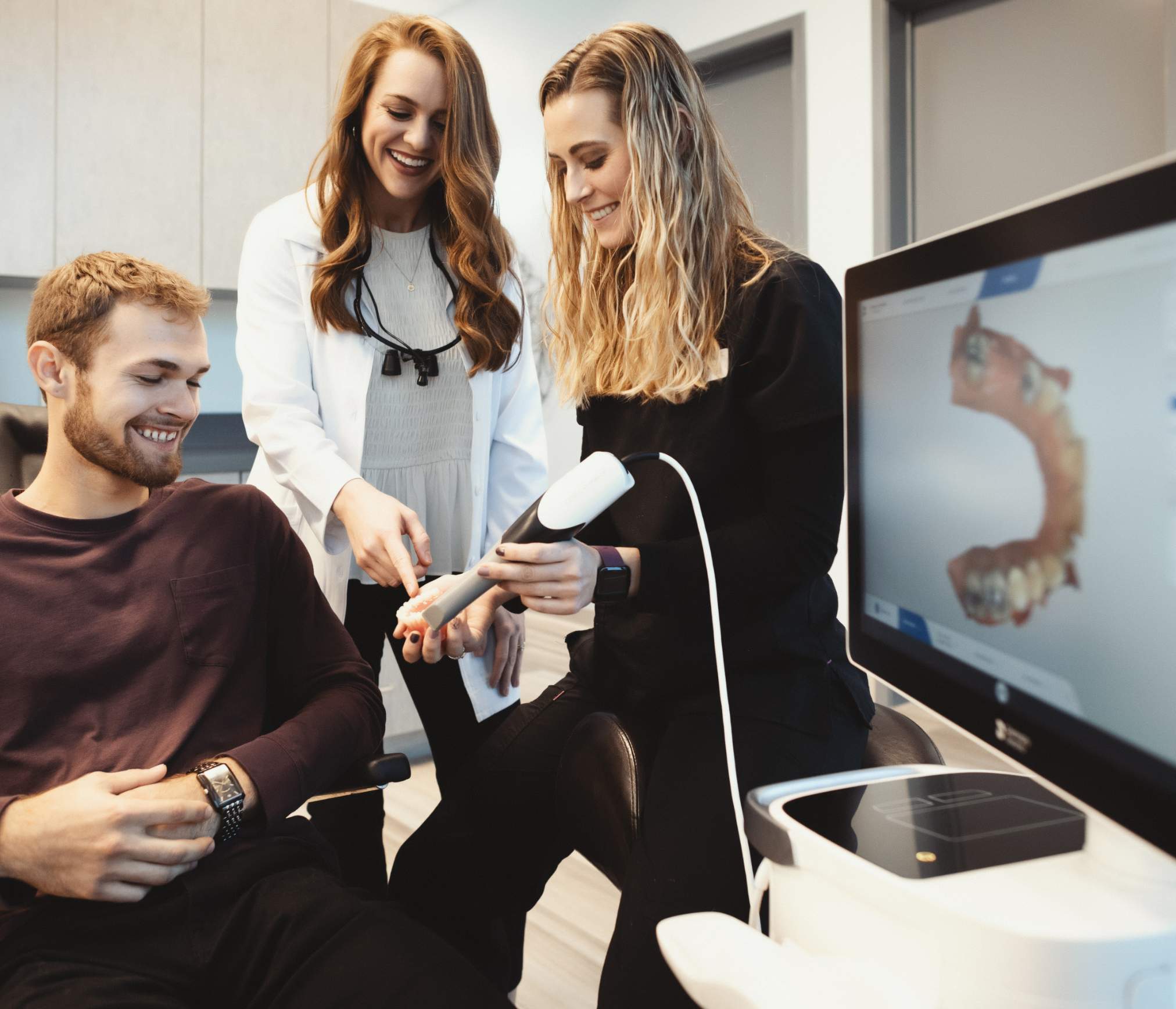 A dentist and team member show a patient a 3D dental scanner