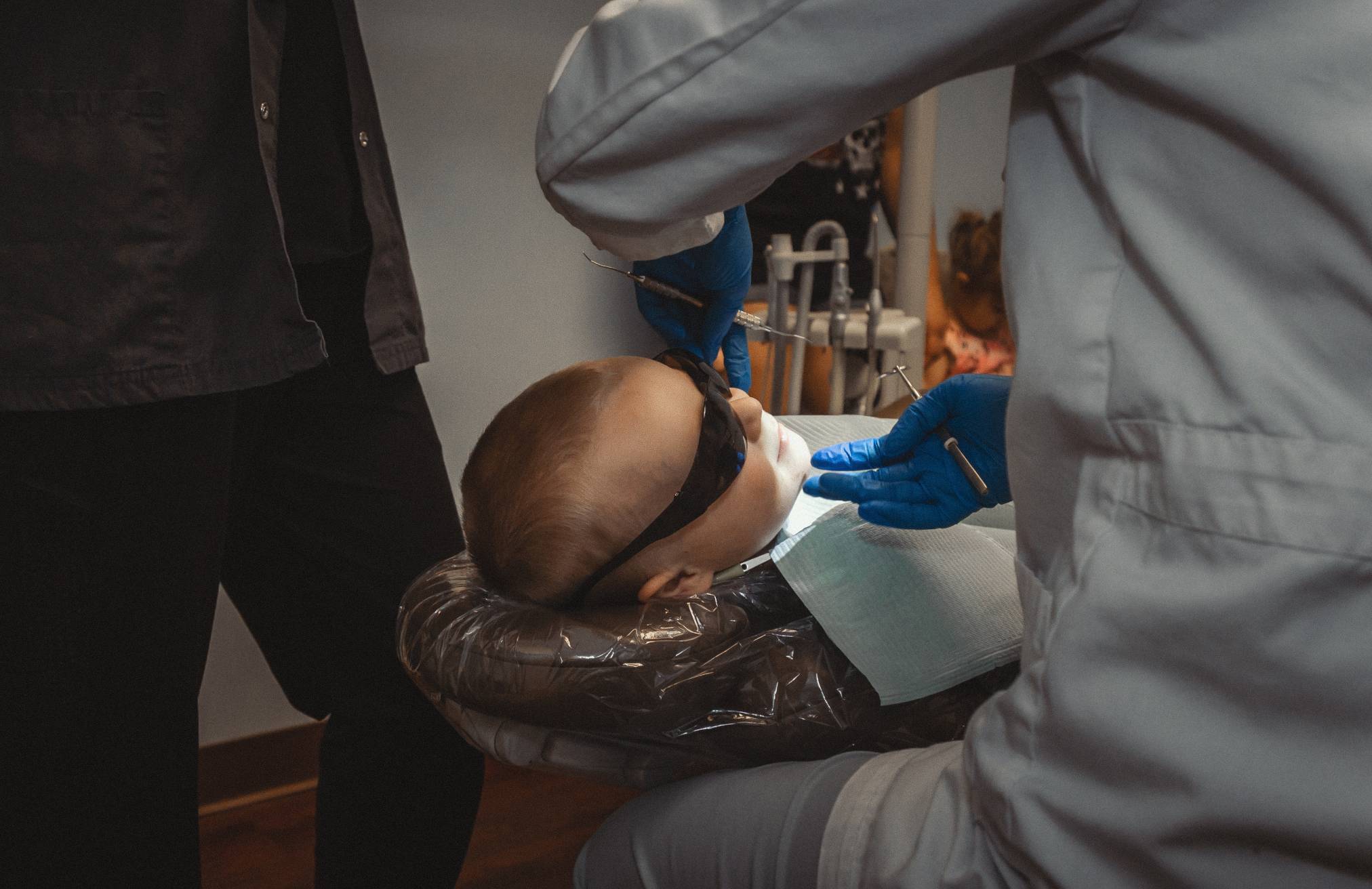 A boy lays back in a treatment chair while a dentist examines his jaw