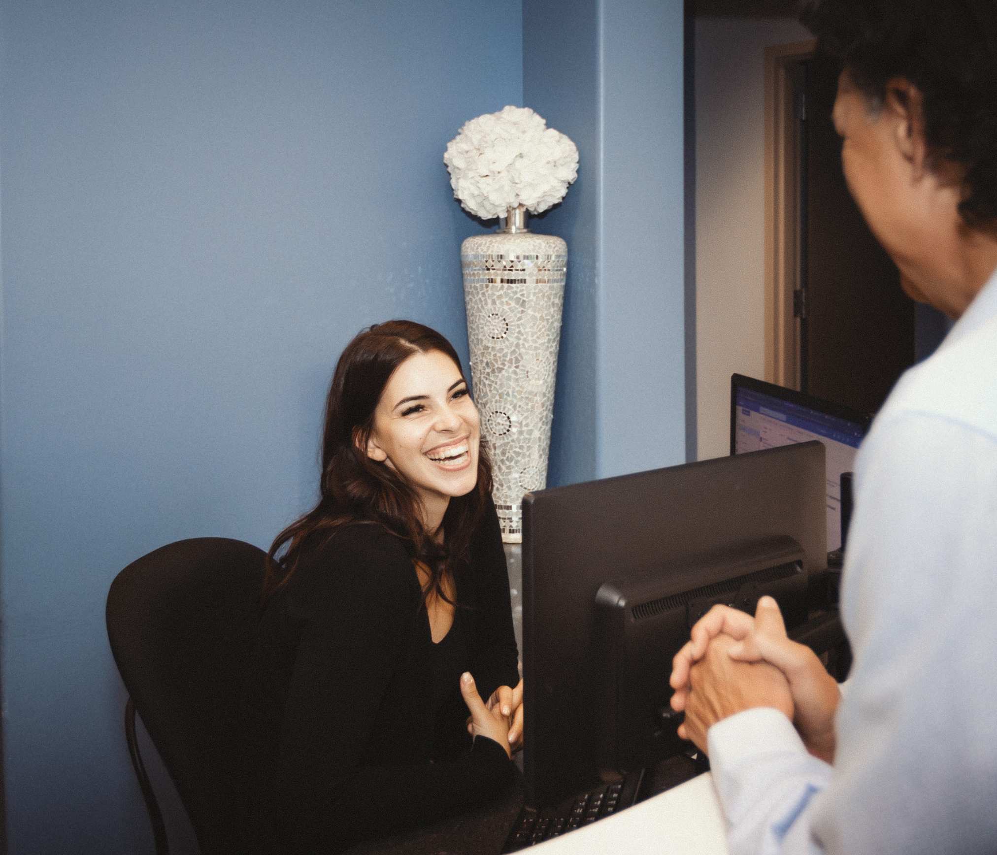 A smiling team member greets a patient from behind the reception desk