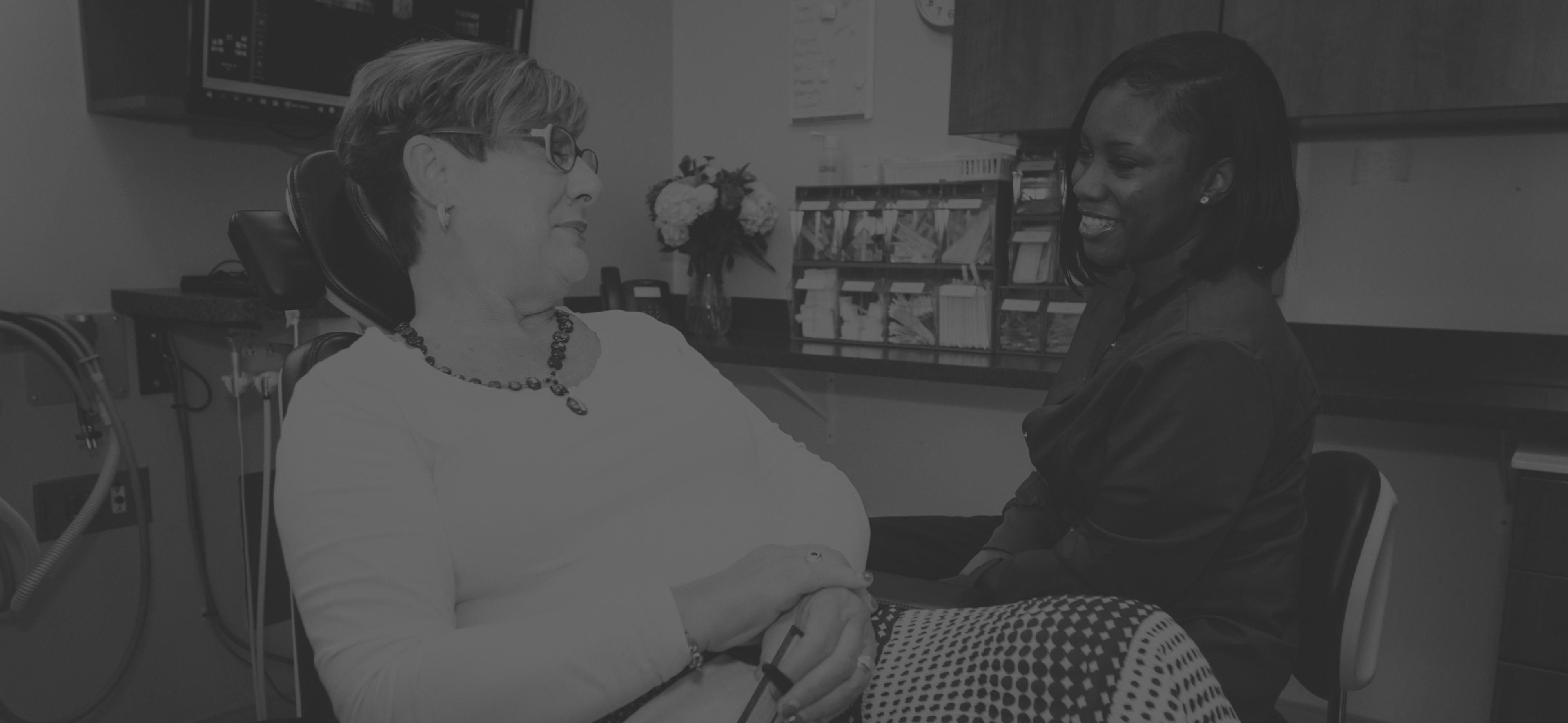 A woman sits in a dental chair and talks with a dentist
