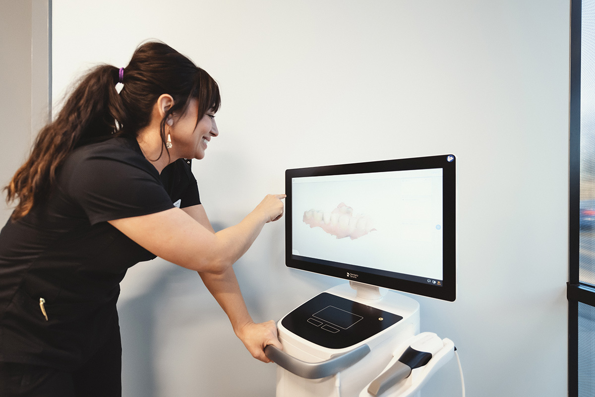 A team member points at a 3D dental scan image on a computer screen