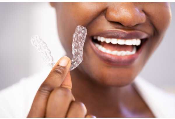 A smiling patient holding a mouth guard in front of their mouth. 
