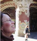 Nainen katsoo hymyillen ylös kauniin, koristeellisen kaarikäytävän vieressä.