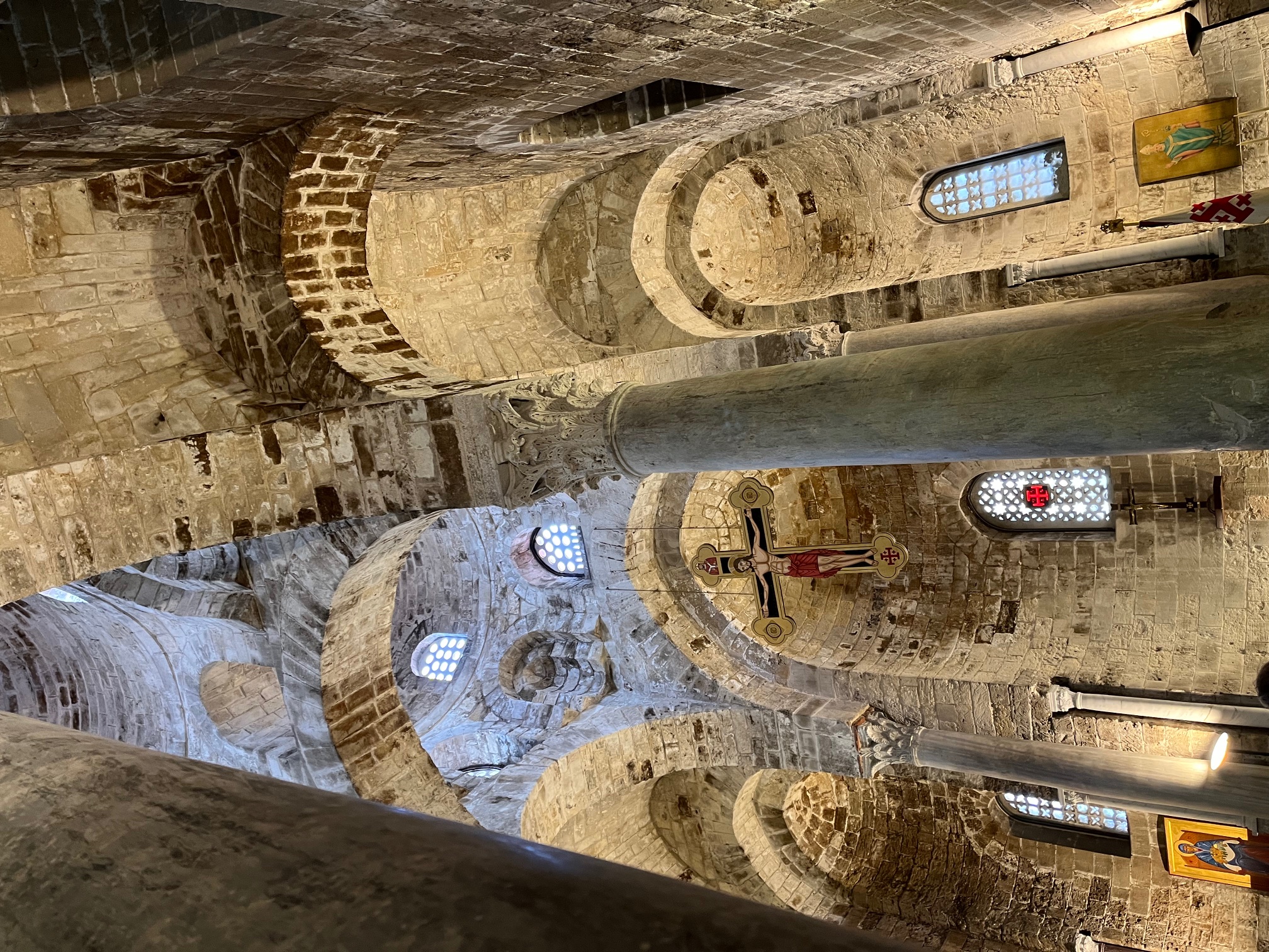 Keskiaikaisen kirkon sisätila, jossa on koristeellisia holvikaaria, kivi- ja marmoripylväitä sekä ristiin naulittu Jeesus -kuva.