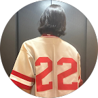 Person with short dark hair seen from behind wearing a beige sports jersey with red stripes and the number 22 in bold red on the back.