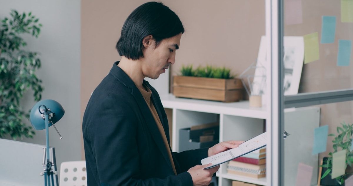 A new life insurance agent reviewing a stack of onboarding documents beside a desk organizer, license paperwork, a calendar with marked training milestones, and a manager pointing to a printed onboarding checklist during a one-on-one review