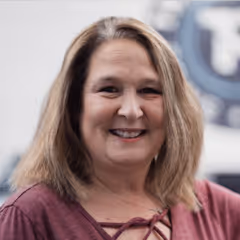 Smiling woman with shoulder-length light brown hair wearing a maroon top.