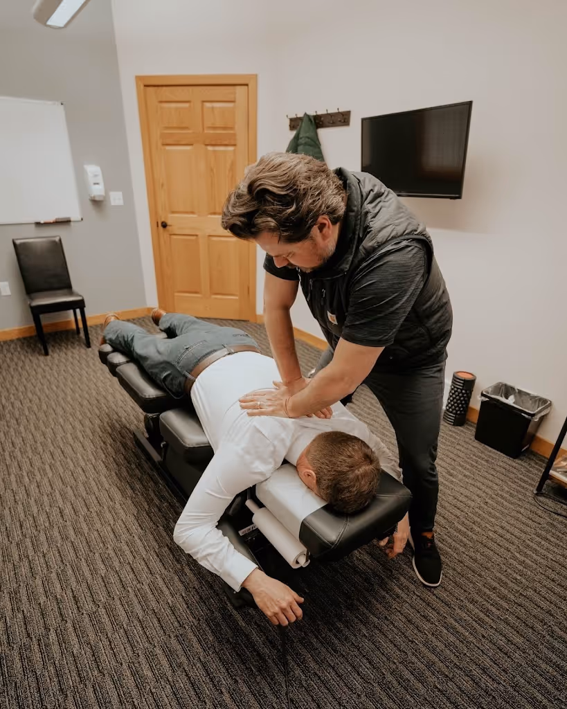 Chiropractor performing back adjustment on a patient lying face down on a treatment table in a clinic.