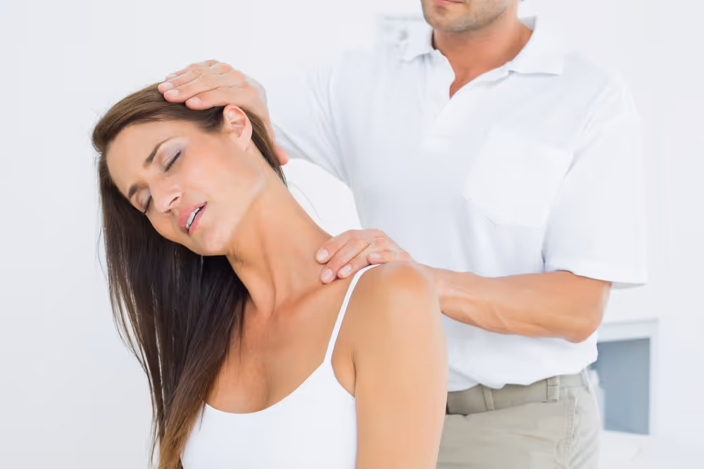 Chiropractor performing neck adjustment on a woman wearing a white tank top.