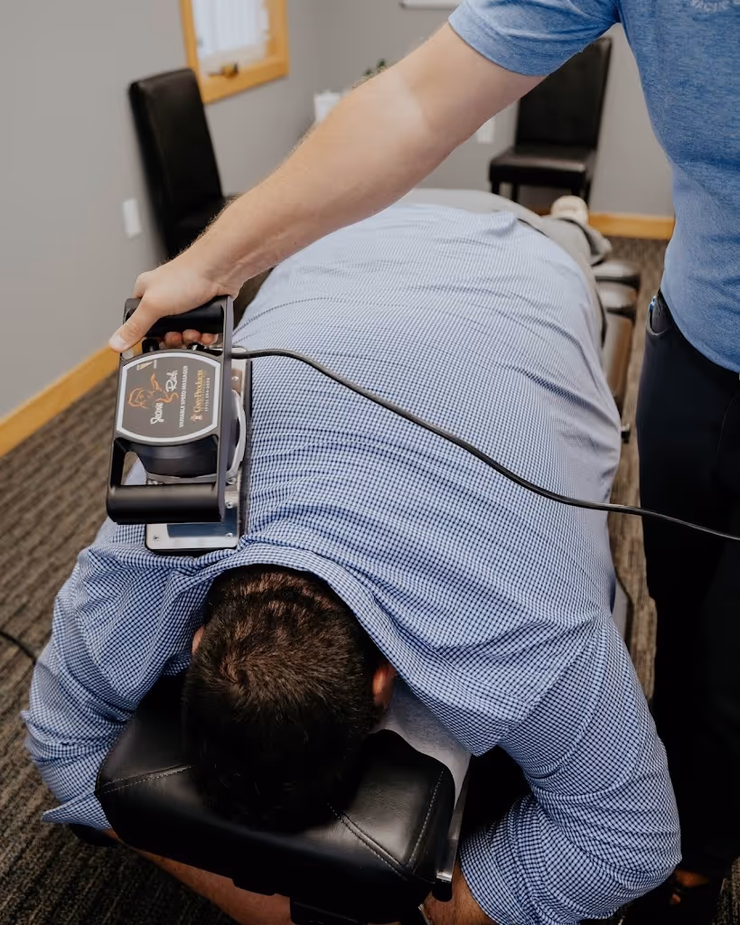 Therapist using an instrument-assisted device on a man's back while he lies face down on a treatment table.