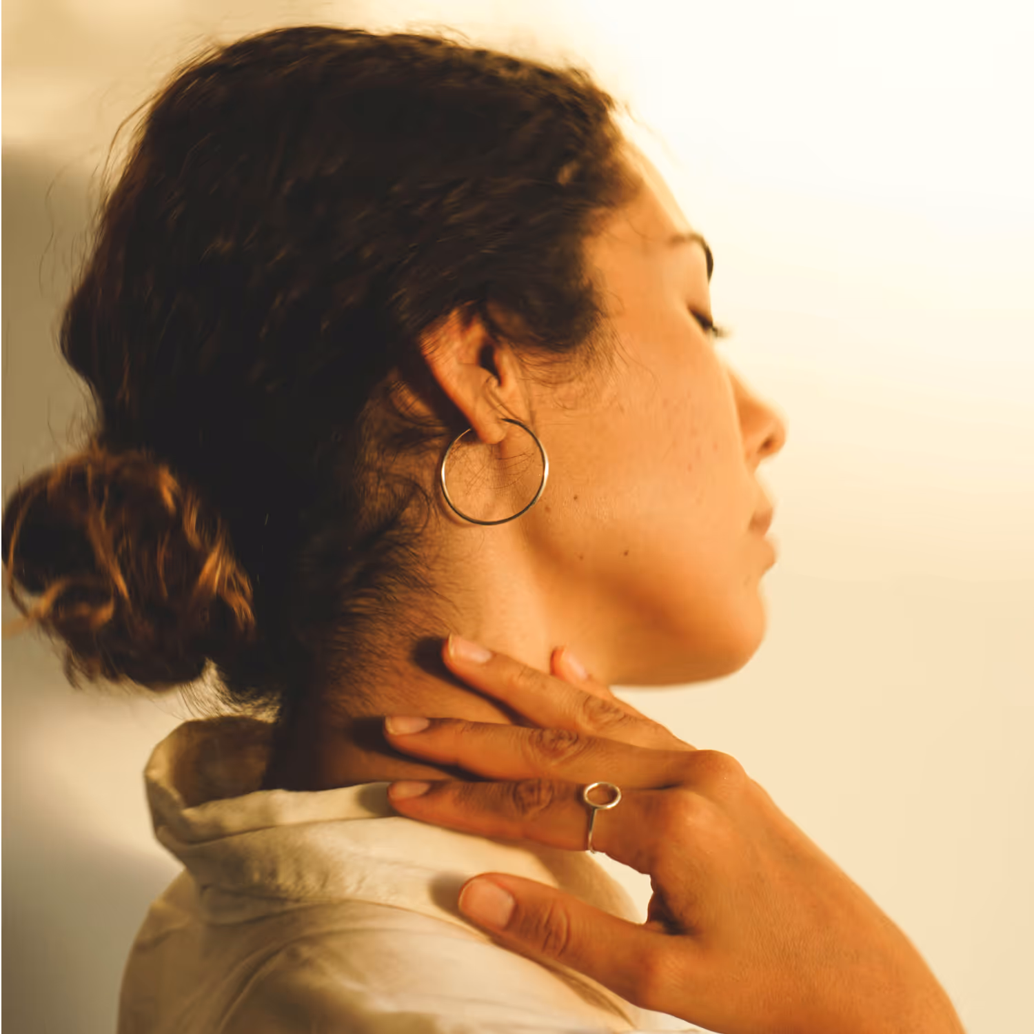 Woman with curly hair in a bun holding her neck with her hand, appearing to have neck pain.