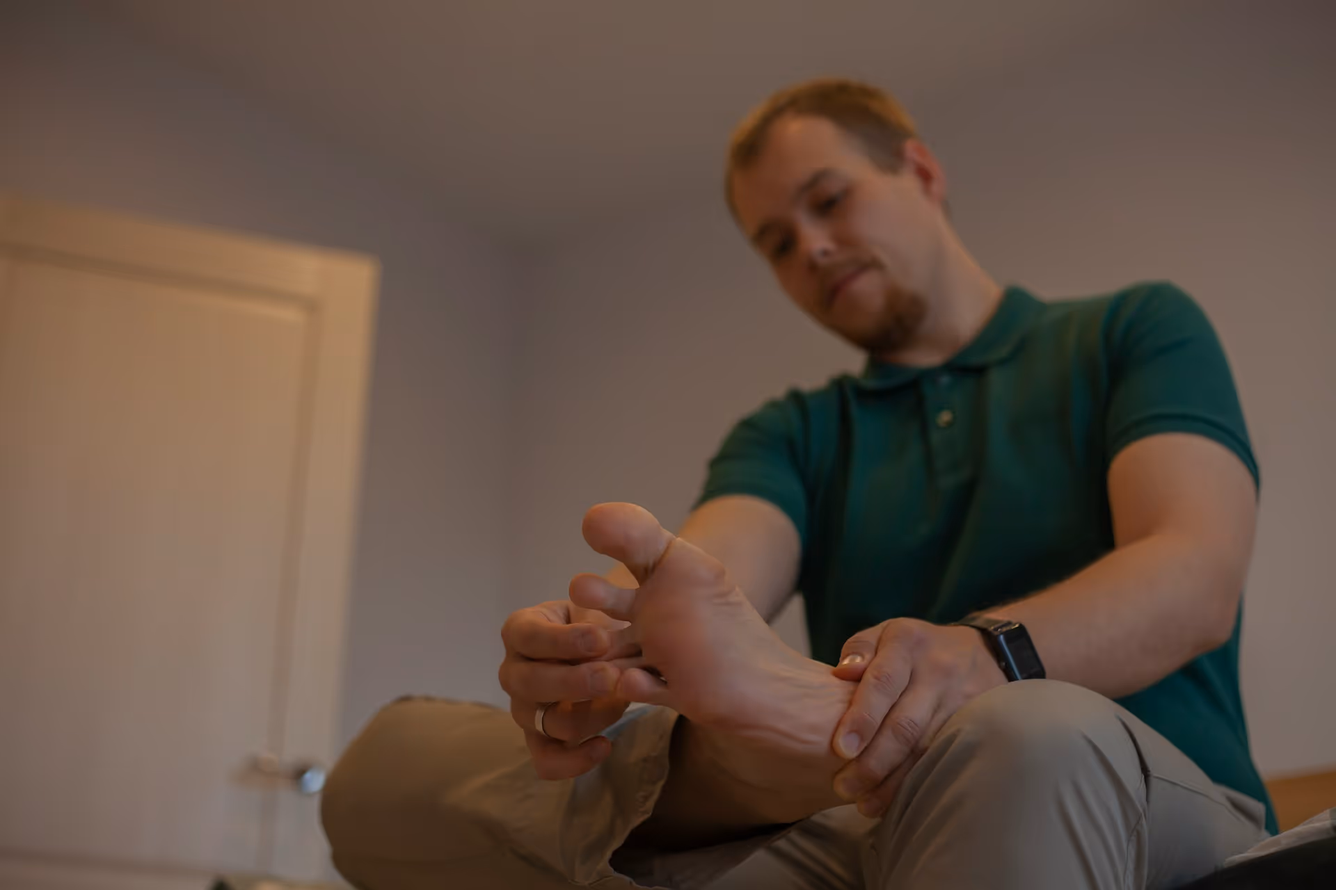 Man sitting on a bed holding and massaging his foot, appearing to relieve foot pain.