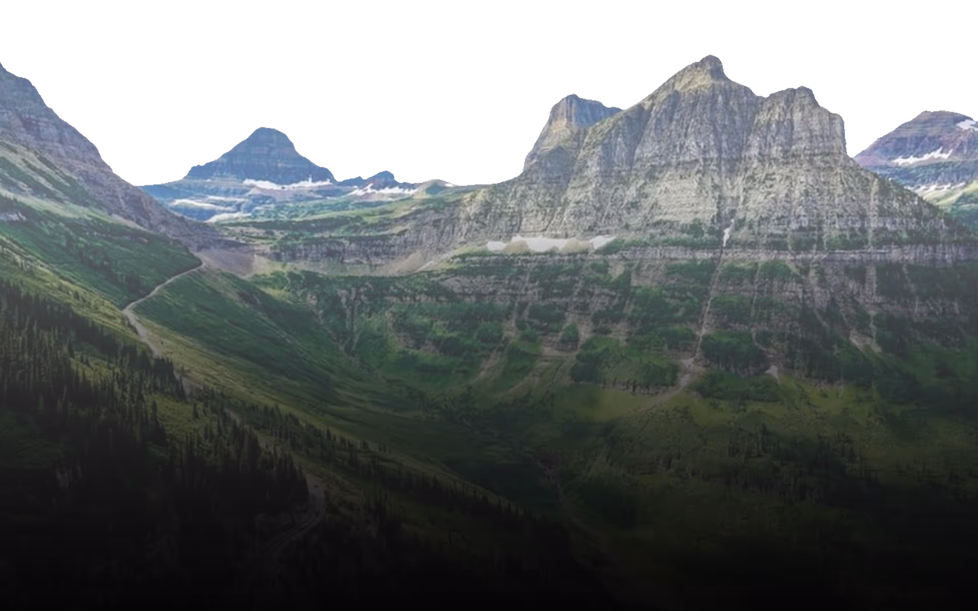 Mountain landscape with rugged peaks, green valleys, and patches of snow under a dark sky.