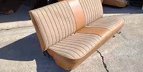 Vintage car bench seat with tan and beige upholstery resting on concrete outdoors.