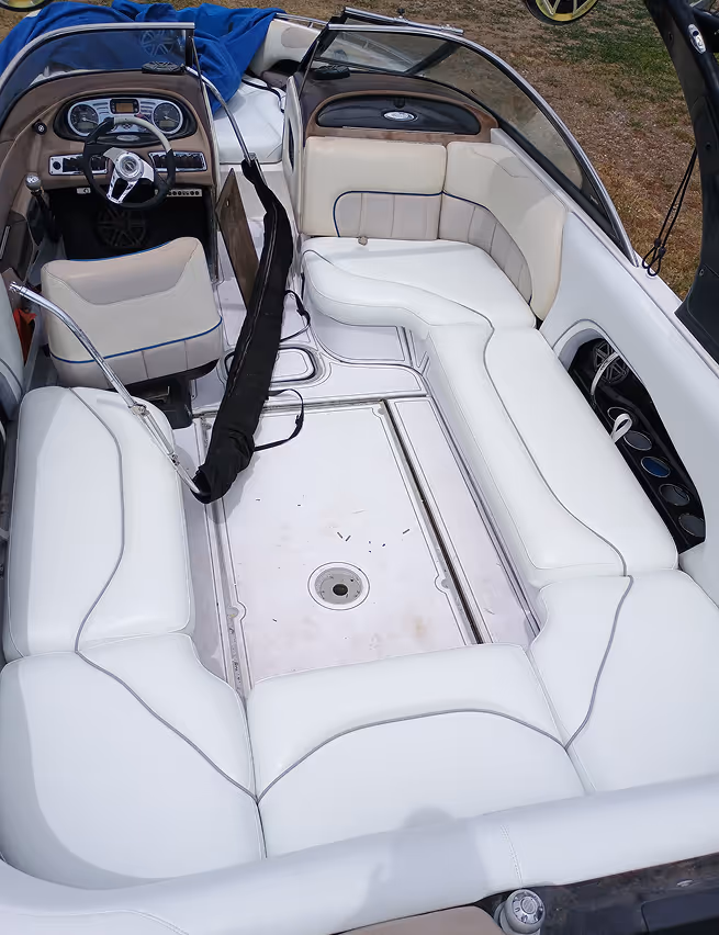 Boat interior with white cushioned wraparound seating and a driver's area with steering wheel and dashboard.