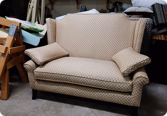 Beige patterned loveseat with rolled arms and two matching cushions set in a cluttered room.