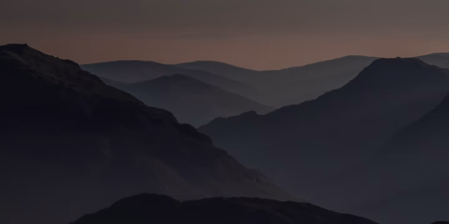 Silhouetted mountain ranges layered under a dusky sky at twilight.