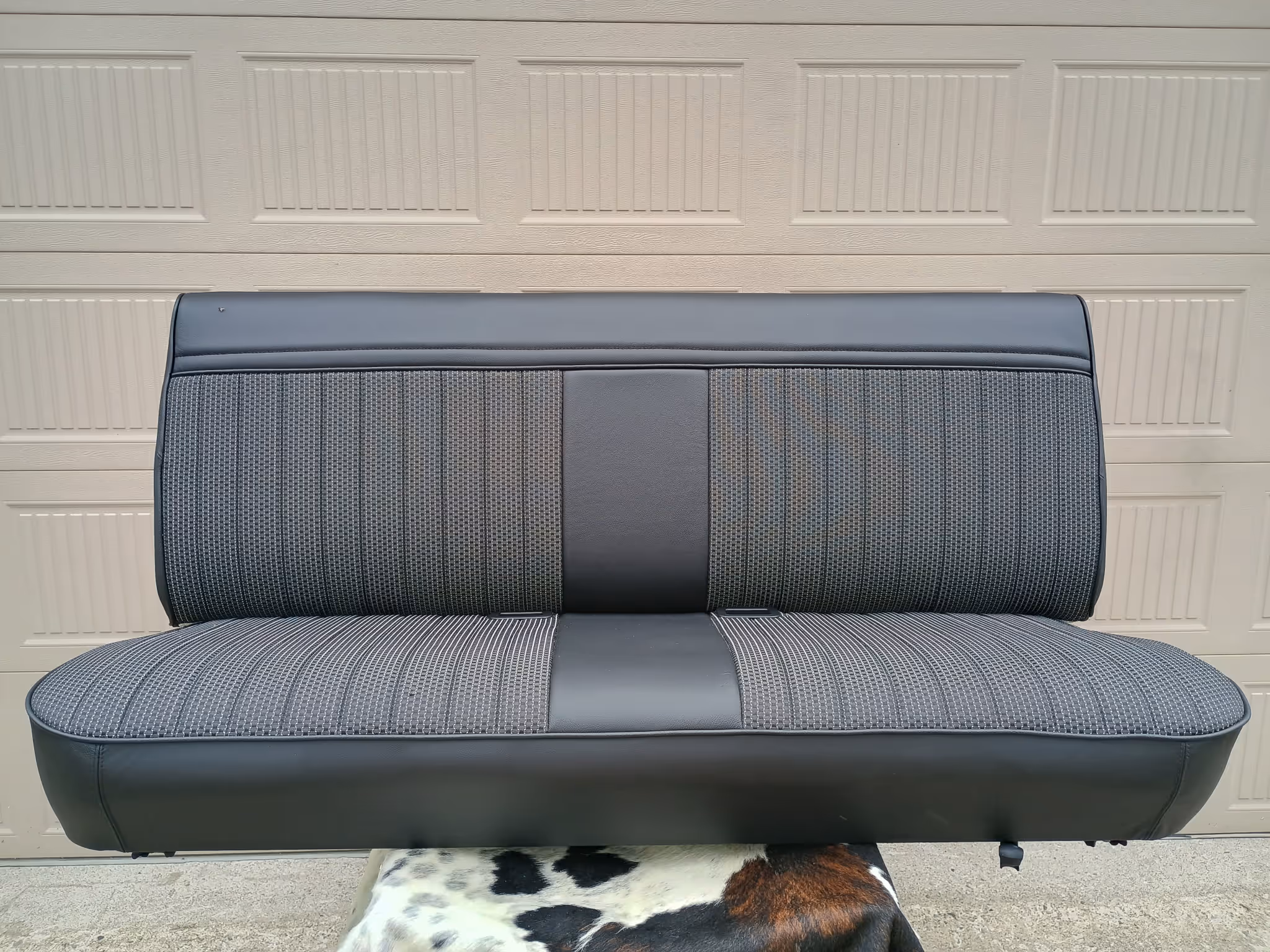 Black and gray truck bench seat with fabric and leather upholstery in front of a beige garage door.