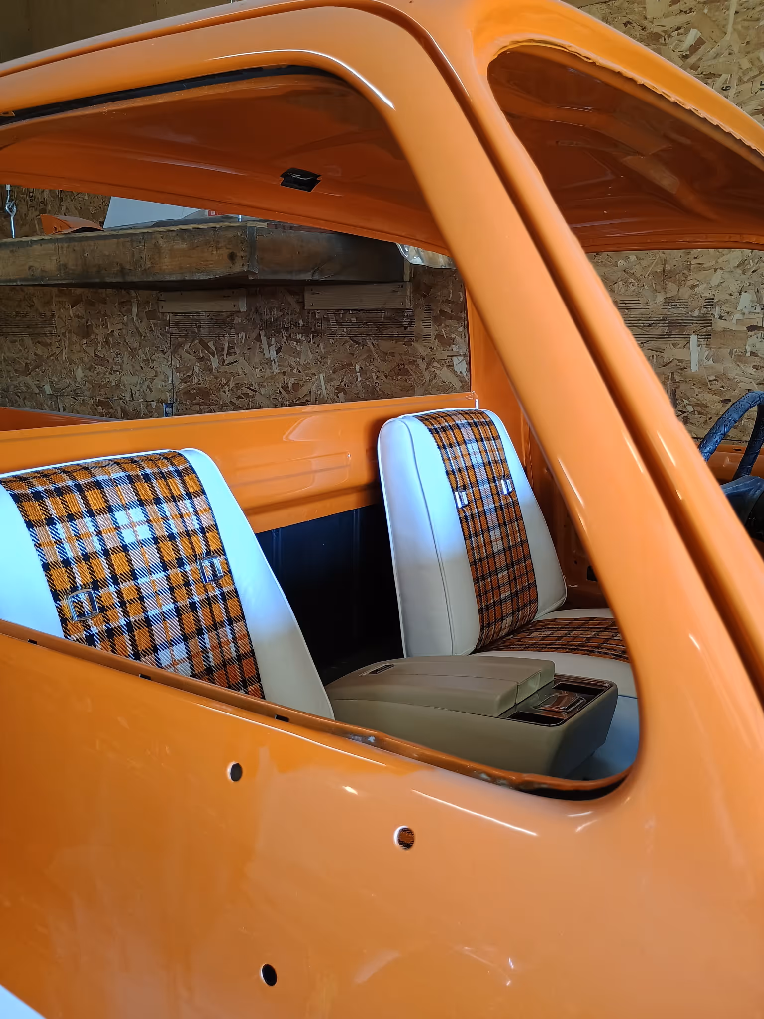 Interior view of an orange vehicle featuring two white bucket seats with orange and black plaid fabric inserts and a beige center console.