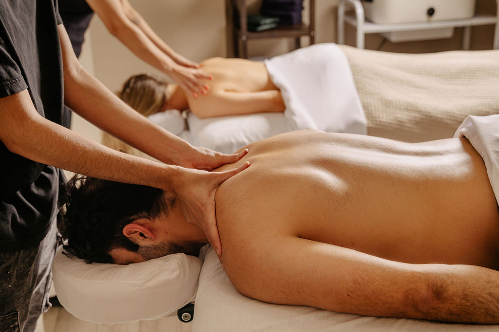 Two people receiving back massages while lying face down on massage tables in a spa setting.
