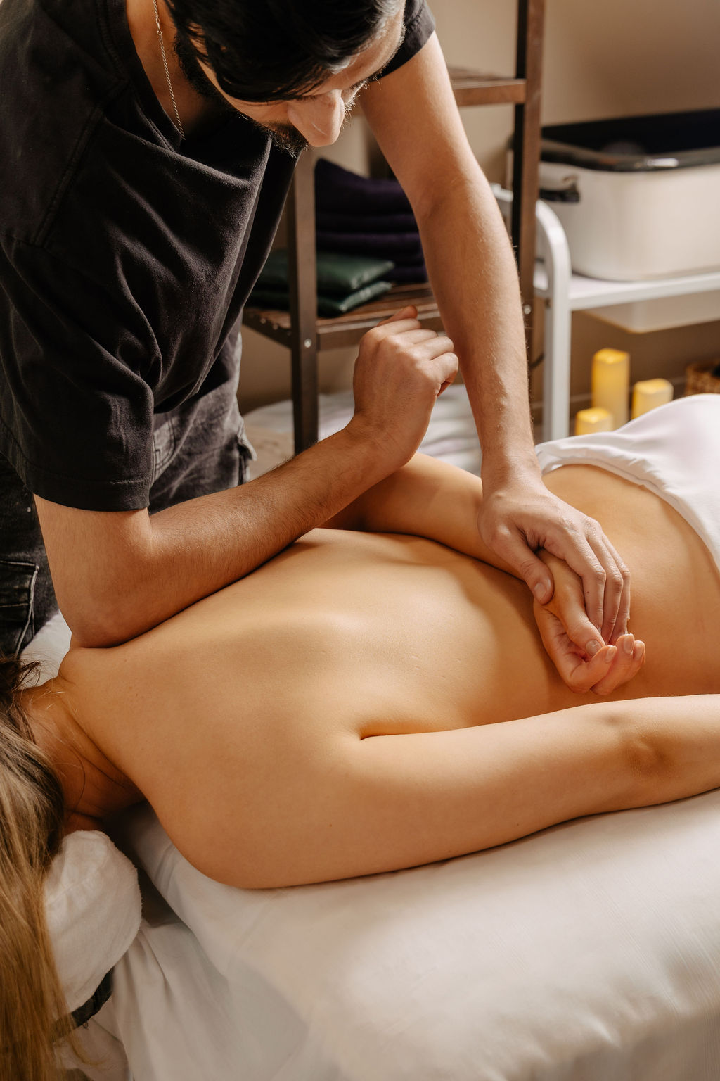 Massage therapist performing an arm and back massage on a woman lying face down on a massage table.