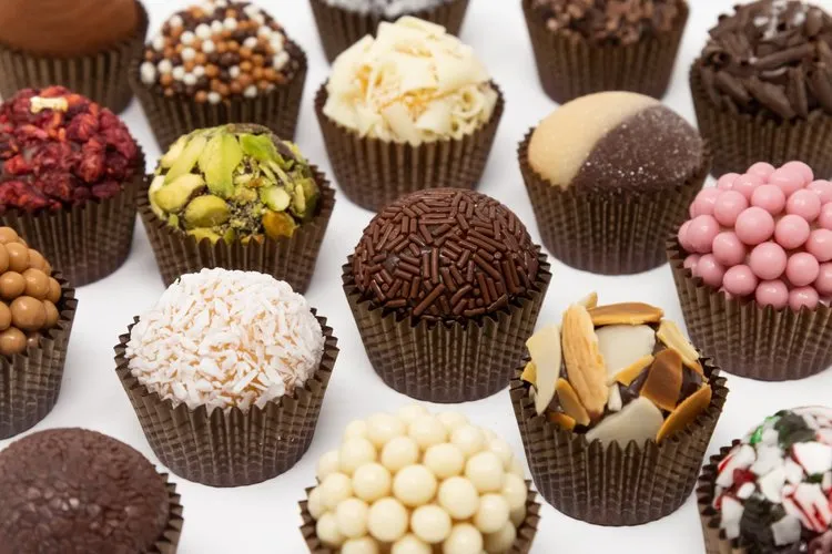Close-up of assorted bite-sized gourmet chocolates decorated with nuts, sprinkles, and candy on a white background.