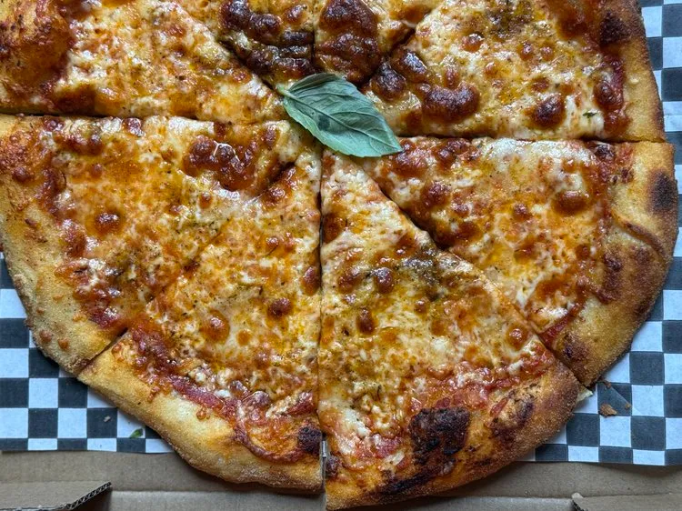 Cheese pizza with a single basil leaf on top, cut into eight slices on checkered paper inside a pizza box.