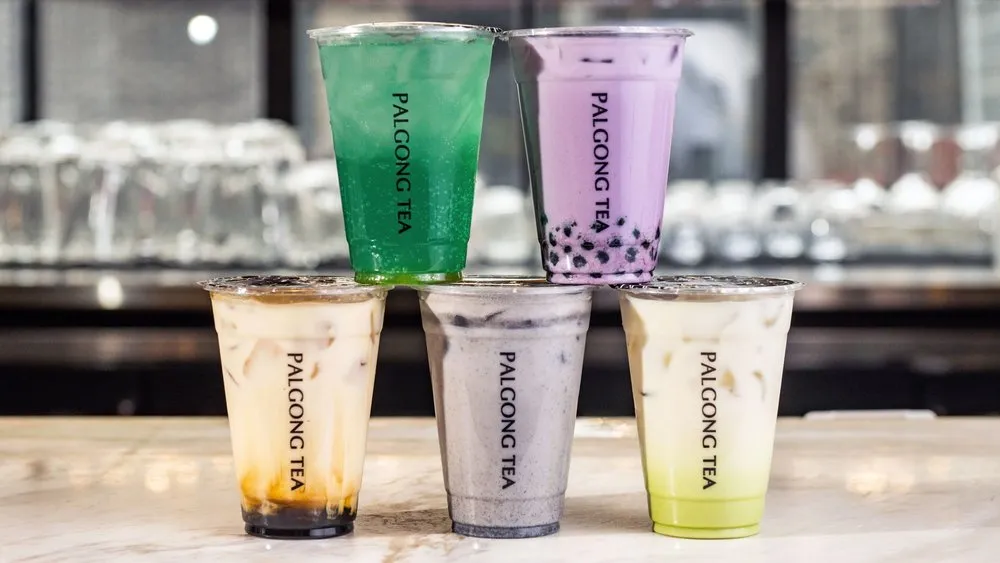 Five colorful Palgong Tea bubble tea drinks stacked in a pyramid on a marble countertop.