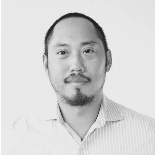 Black and white headshot of a man with short hair and a goatee wearing a striped collared shirt.