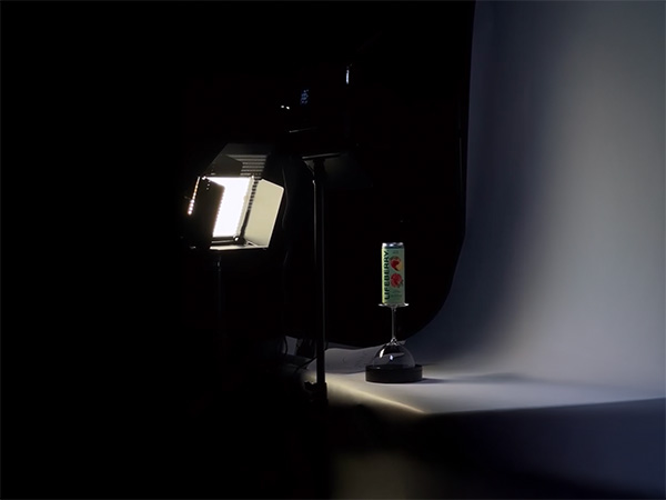 Photo studio setup with a spotlight illuminating an upside-down can on a stand against a curved white backdrop.
