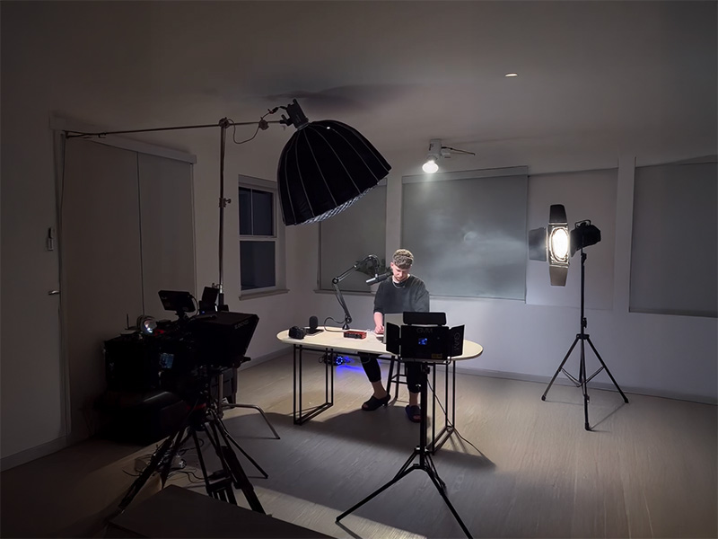 Man sitting at a desk in a studio surrounded by professional lighting and camera equipment.