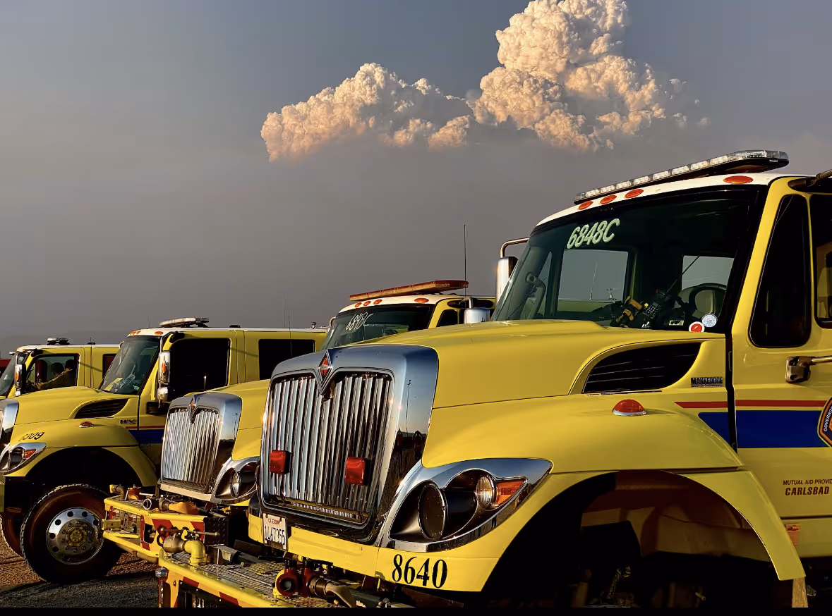 Row of yellow fire trucks parked outdoors under a cloudy sky.