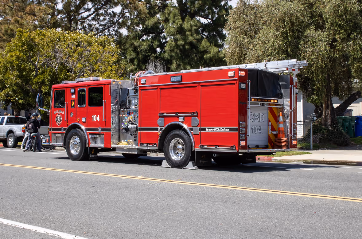 Side view of a red fire truck numbered 104 parked on a street with two people standing nearby.