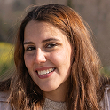 Smiling young woman with long brown hair outdoors in natural daylight.