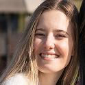 Young woman with long blonde hair smiling outdoors.