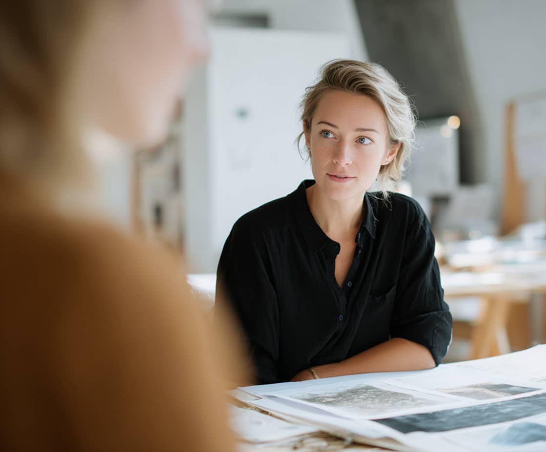 A woman in a black shirt attentively listening during a meeting at a table with documents.