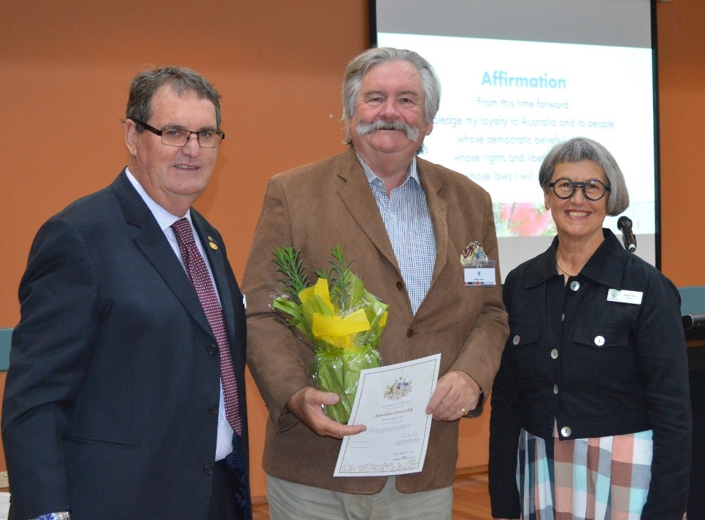 Man holding certificate and plant, standing next to another man and woman.