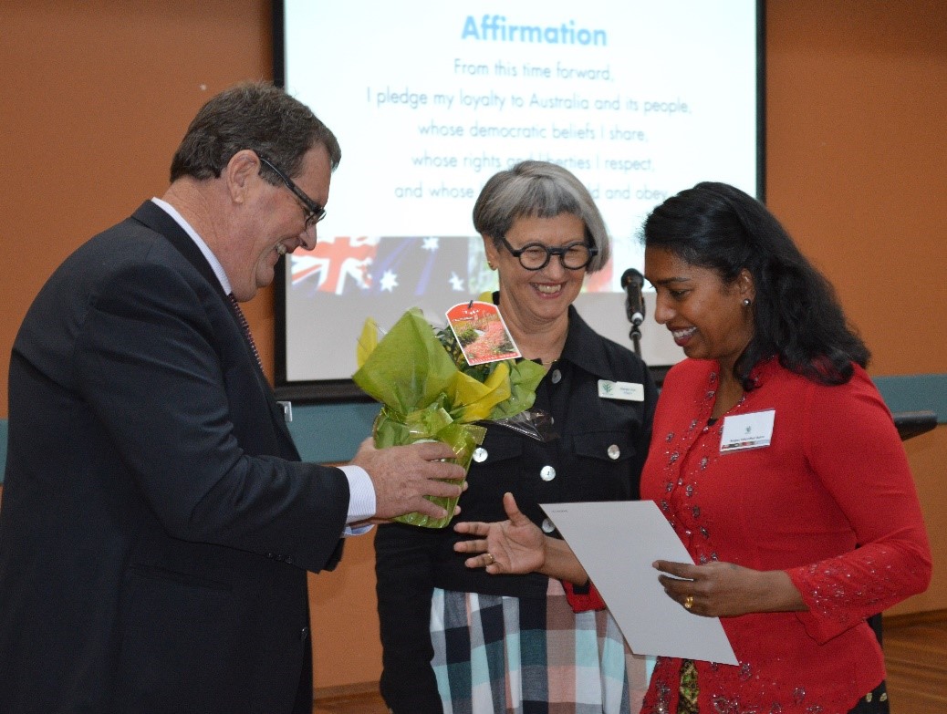 A woman being handed a certificate and plant as two people look on.