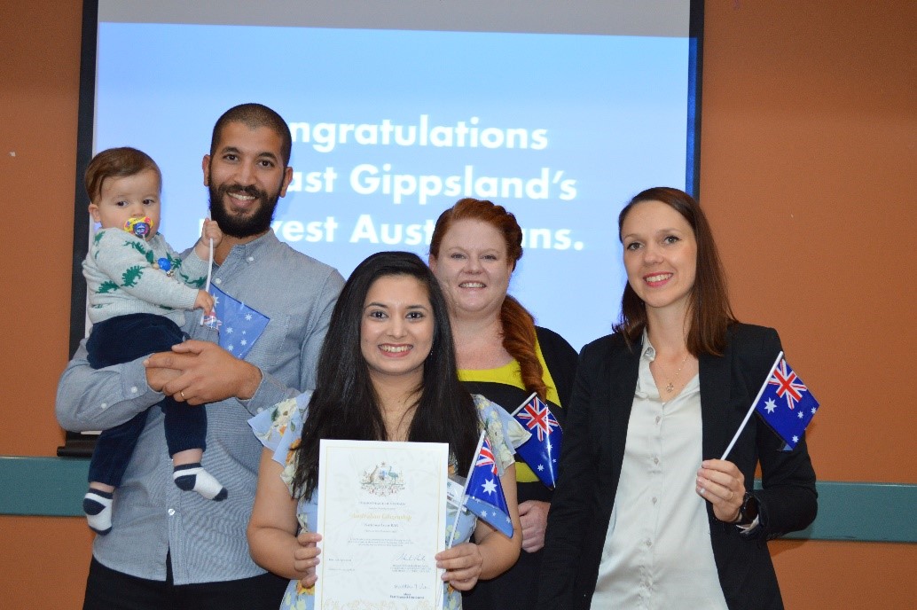 Woman holding certificate standing with four others, holding Australian flags.