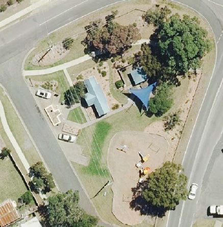 An aerial photo of a small park with trees, a shade sail and a building.