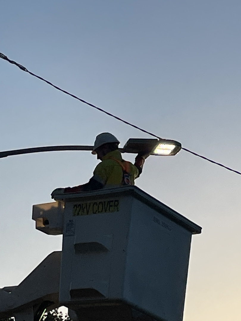 A worker in high vis and hardhat in a an elevated box checking a streetlight at dusk.