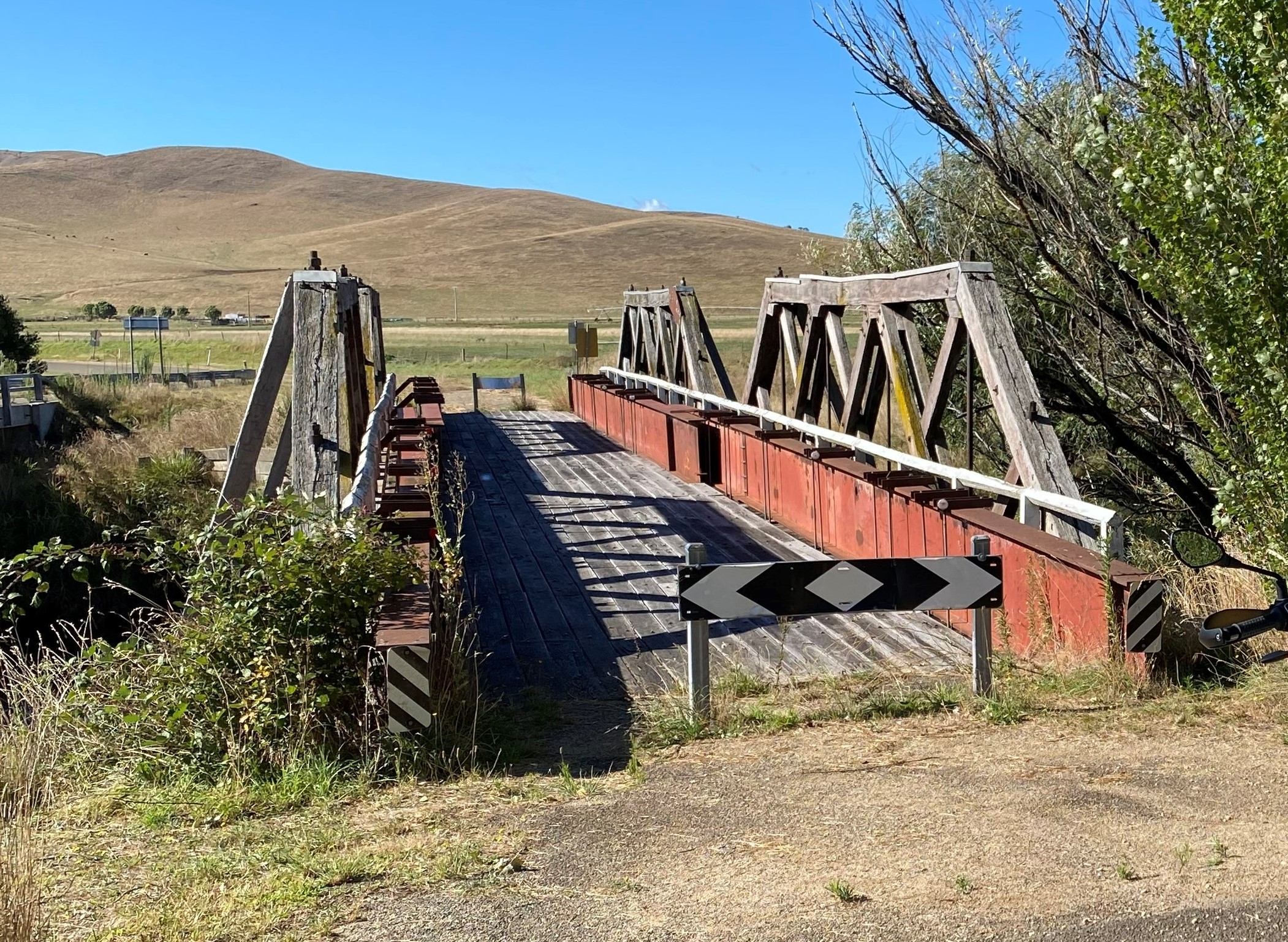 Small, old timber bridge with bald hill in the background.