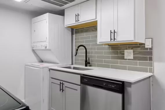 kitchen with sink, dishwasher, and stacked laundry machines