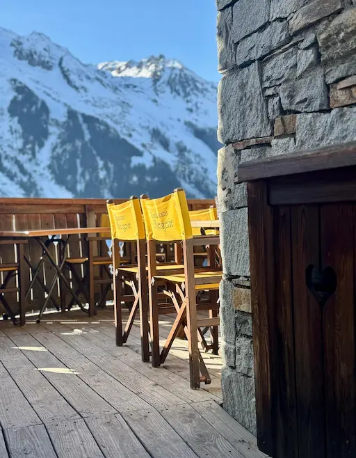 Terrace of the "Restaurant La Bergerie," with tables and yellow chairs facing a panorama of snowy alpine peaks.