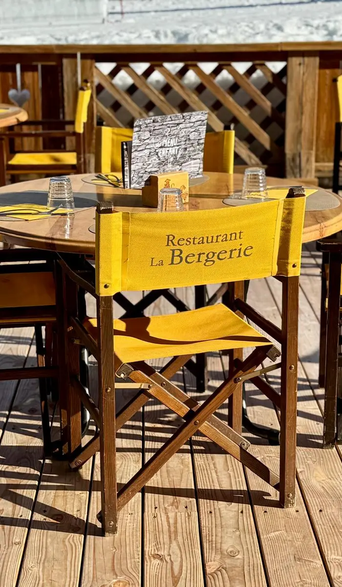 Rustic, dark, and warm chalet interior, with a large stone and wood fireplace in the center, and fur seating.
