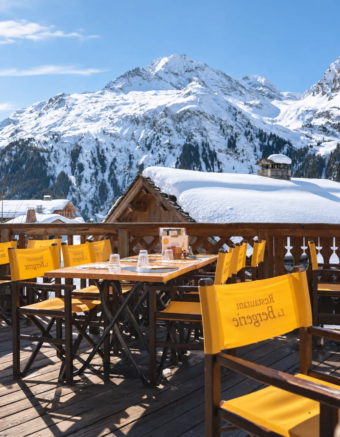 Terrace of the "Restaurant La Bergerie," with tables and yellow chairs facing a panorama of snowy alpine peaks.