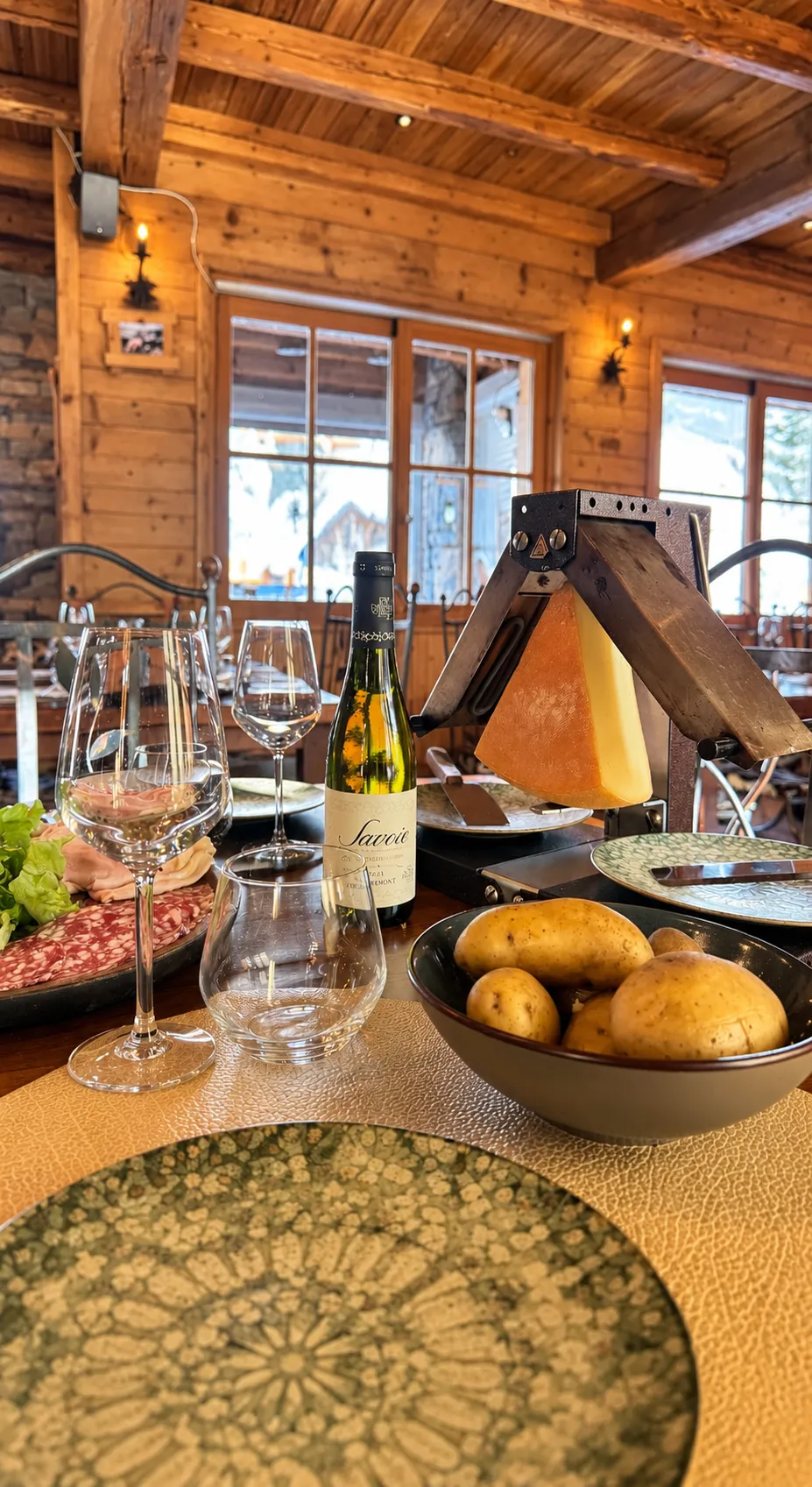 Rustic interior, long table set with wine glasses, bench with cushions along a dry stone wall, and decorative niche with white fur and wood.